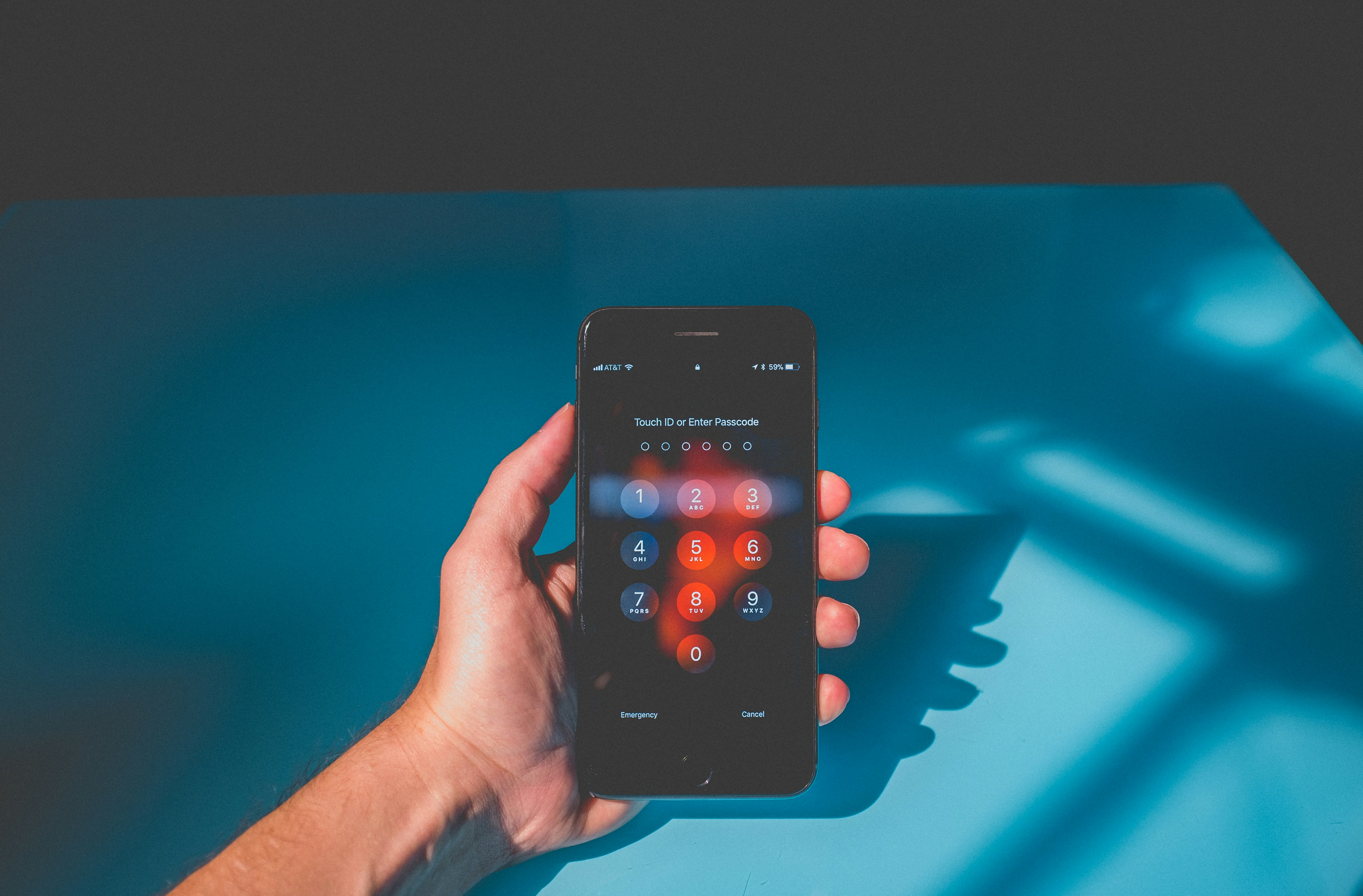 Fotografie einer Hand, die vor einem blauen Hintergrund ein Smartphone hält. Das Smartphone zeigt den Eingabebildschirm für den Freischaltcode.